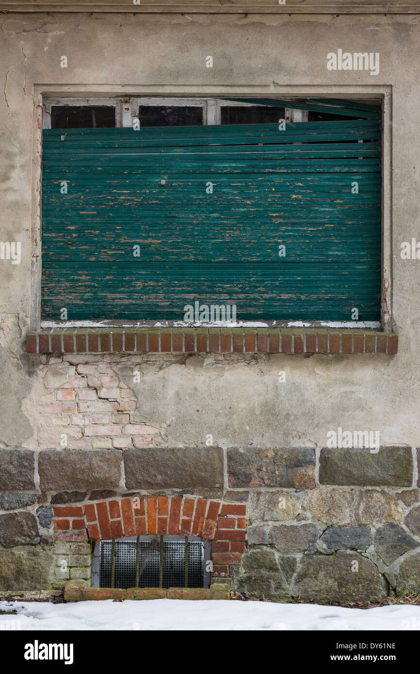 Turquoise cassée sur un des volets vieille maison en décomposition dans l'hiver de l'Europe. Banque D'Images