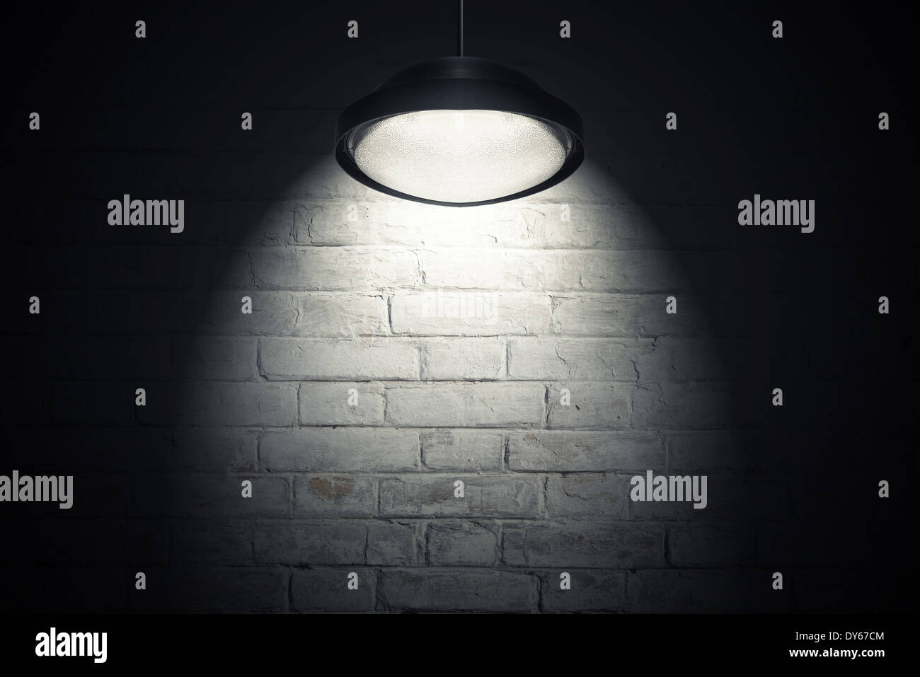 Mur en brique blanche illuminée de spot light à partir de la lampe de plafond. L'intérieur sombre en arrière-plan avec l'exemplaire de l'espace. Banque D'Images