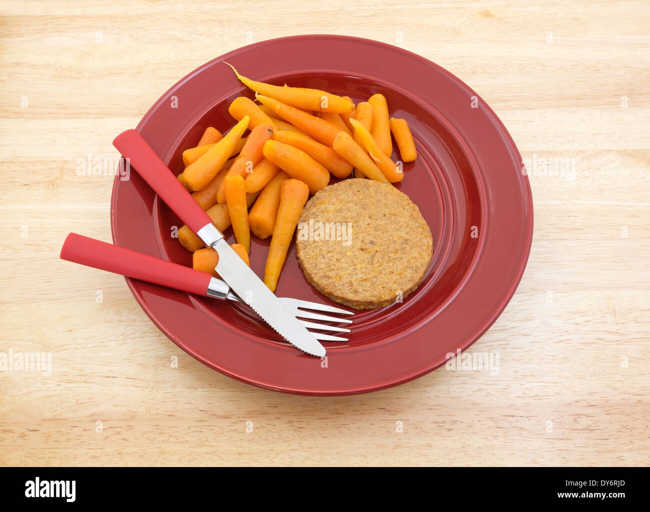 Un régime alimentaire d'un repas vegetable burger avec des carottes sur une plaque rouge avec l'argenterie au sommet d'une table en bois. Banque D'Images