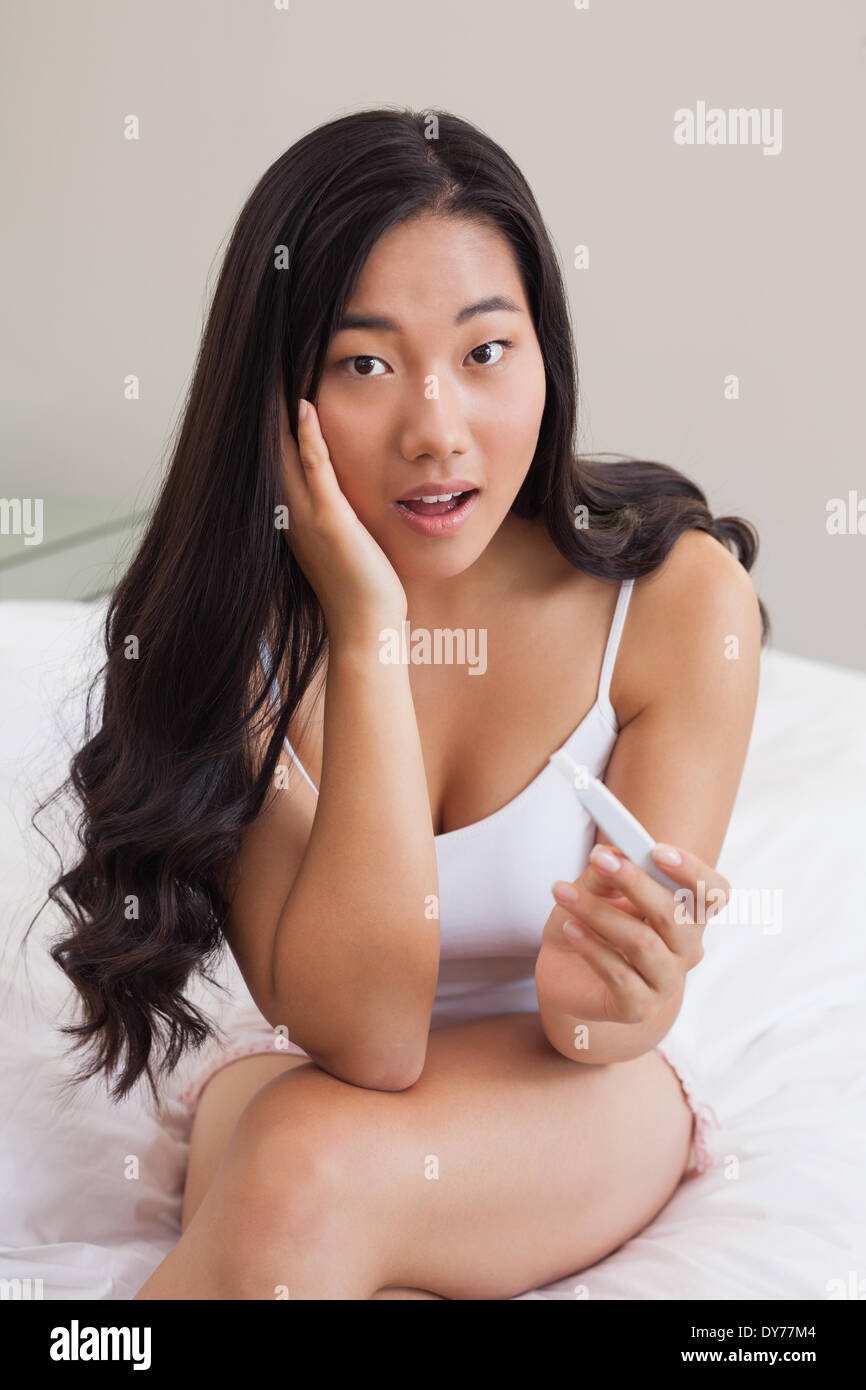 Choqué woman sitting on bed holding test de grossesse Banque D'Images