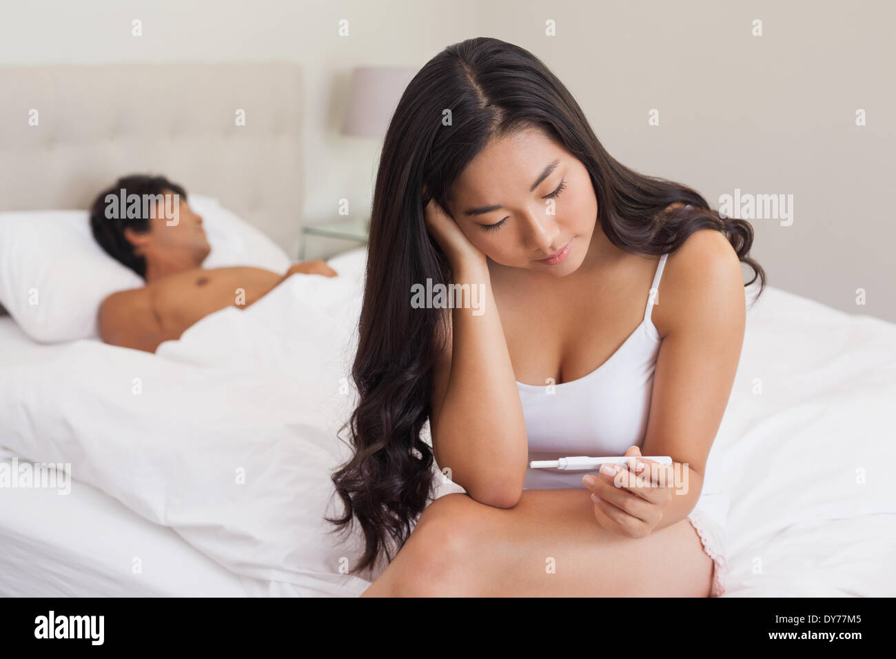 Woman sitting on bed holding test de grossesse comme petit ami sleeps Banque D'Images