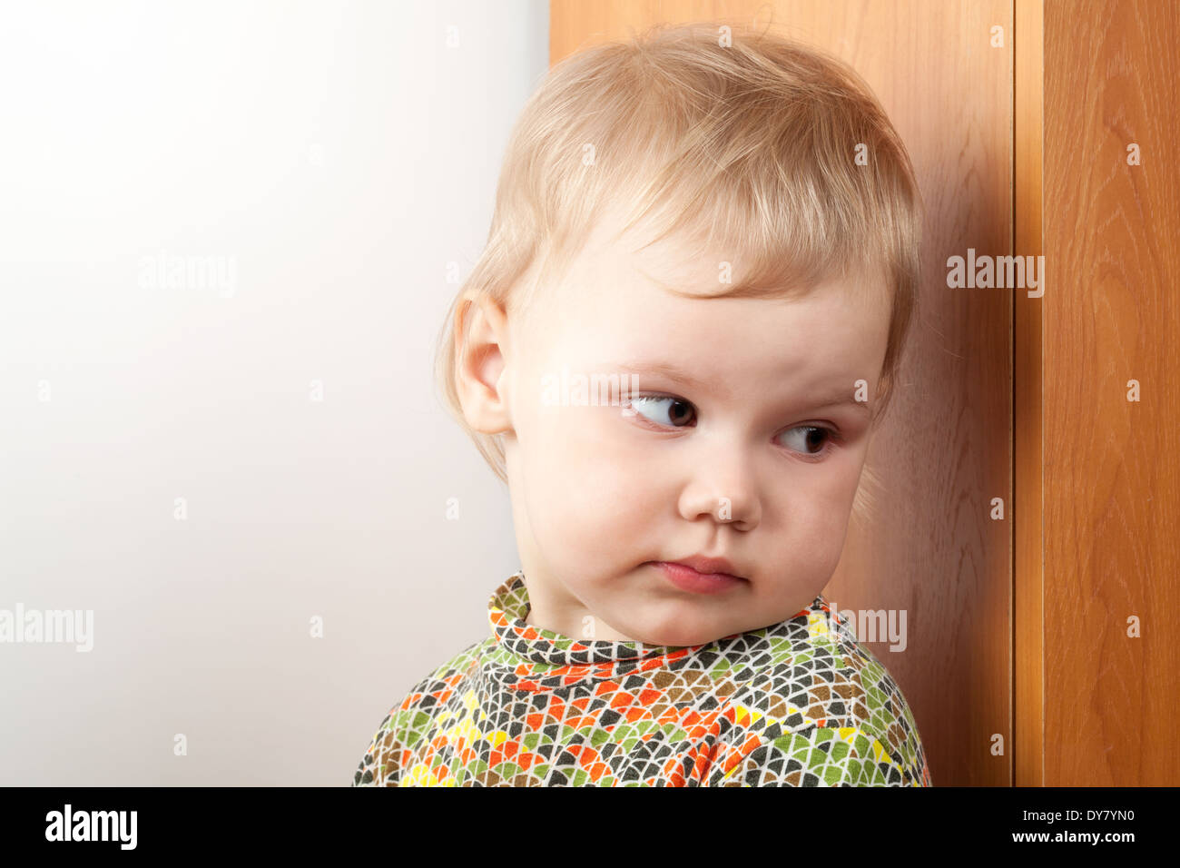 Peu Caucasian baby girl se cacher derrière un placard Banque D'Images