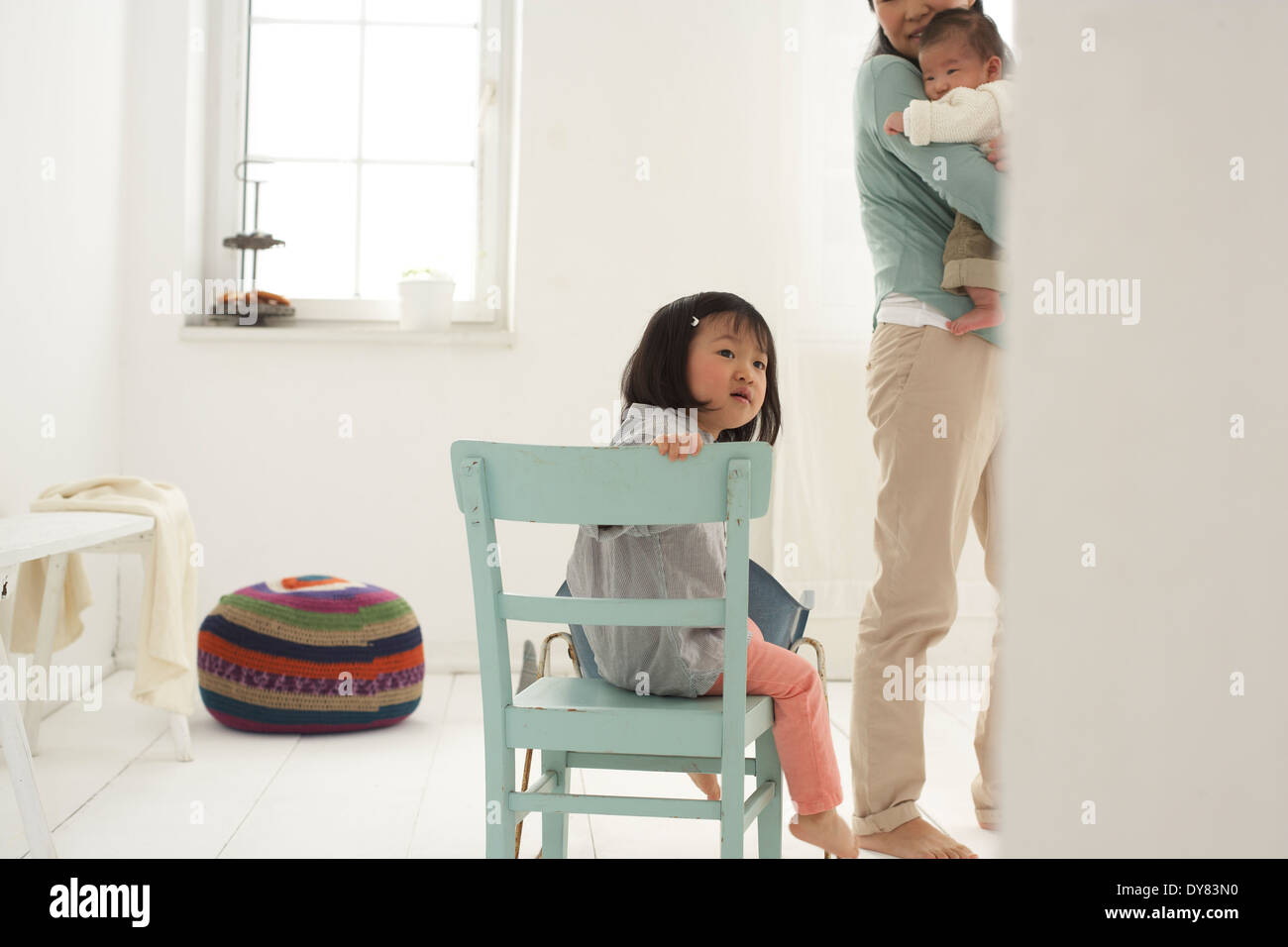 Petite fille asiatique assis sur une chaise, mère et sœur dans l'arrière-plan Banque D'Images