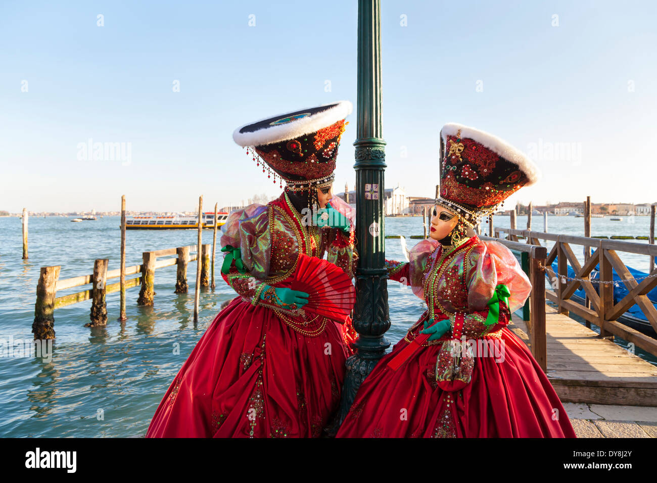 Carnaval de Venise - deux femmes en beau rouge fancy dress costumes, masques et chapeaux posent par la lagune, Carnevale di Venezia, Italie Banque D'Images