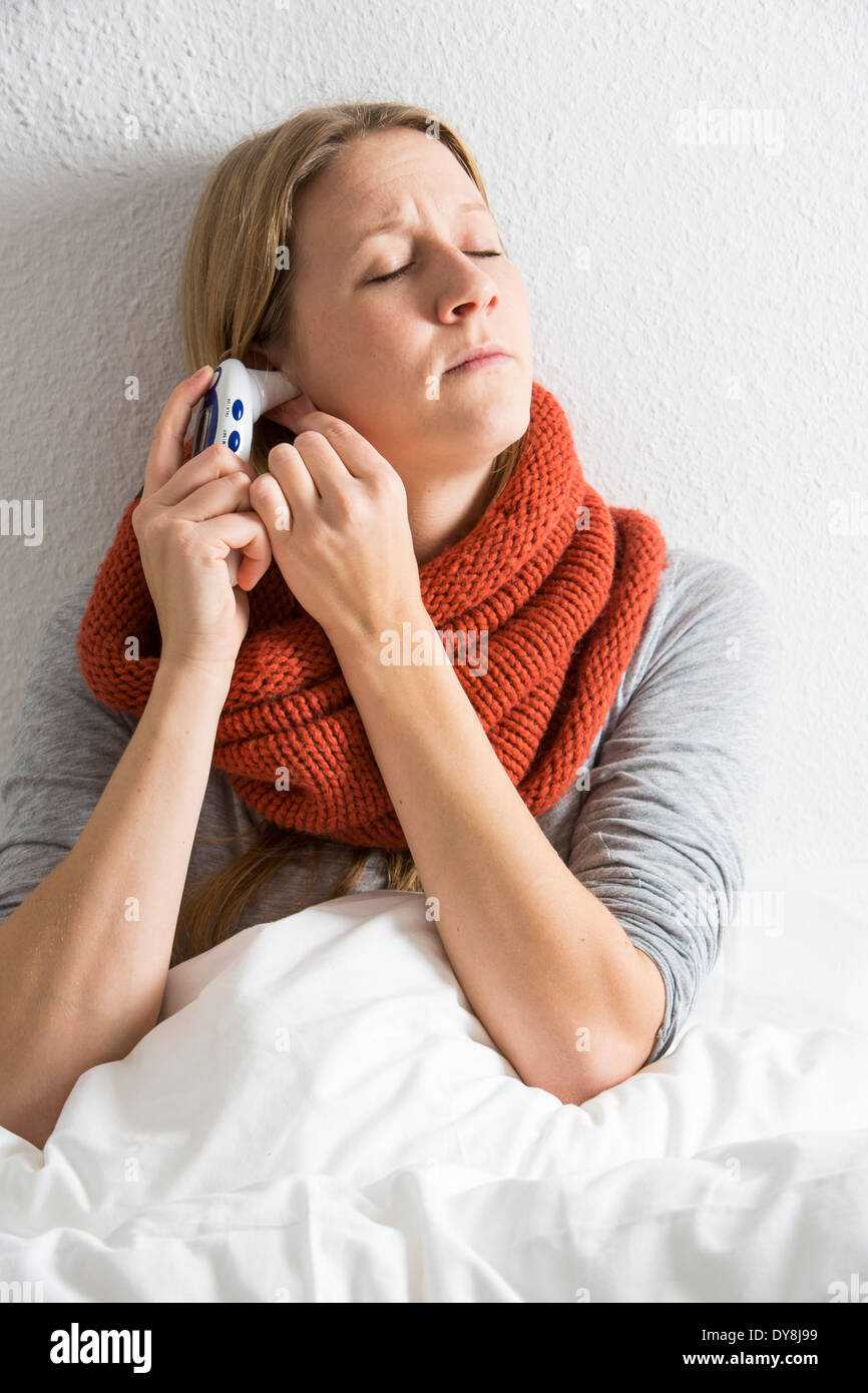 Jeune femme au lit, a un rhume, fièvre, grippe, fièvre, mesurée avec un thermomètre numérique Banque D'Images