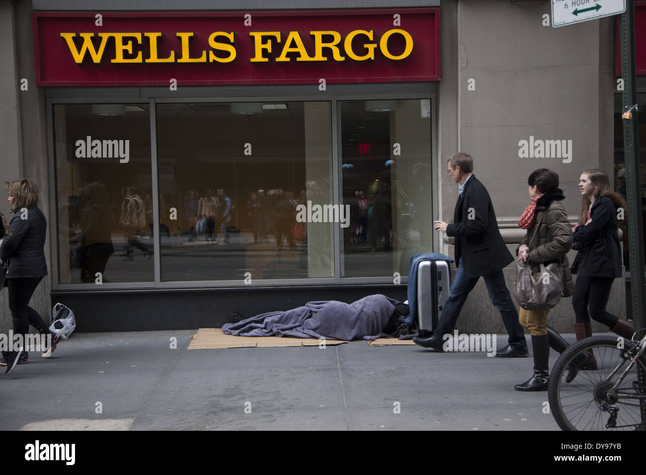 Les gens à pied, en remarquant à peine, une personne sans-abri dormant en face d'une banque dans le centre de Manhattan. Banque D'Images