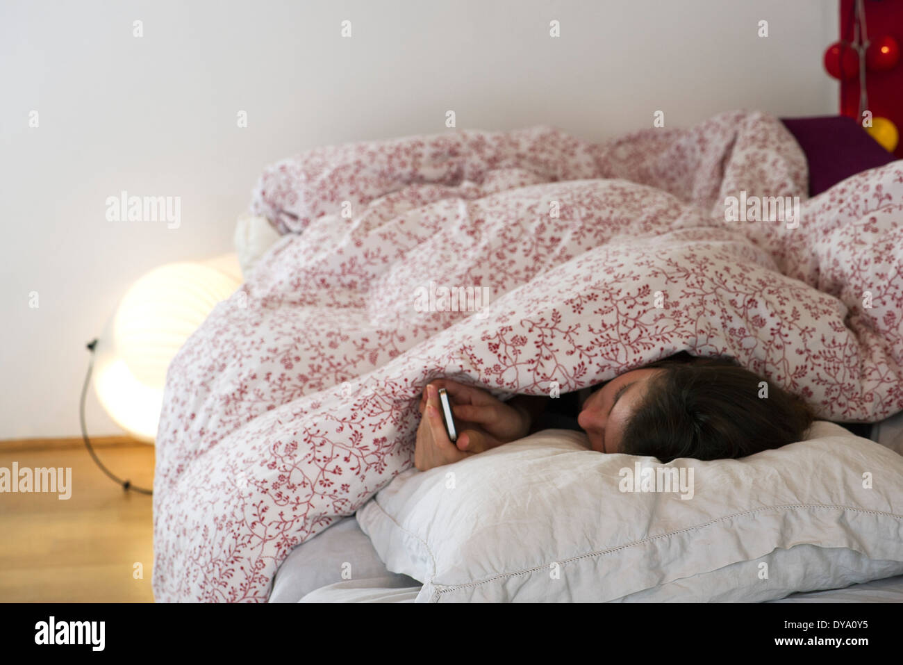Femme au lit sous les couvertures, looking at smartphone Banque D'Images