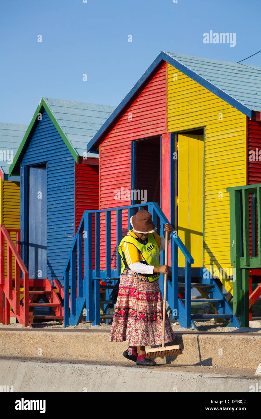 Une balayeuse nettoie le chemin en face de l'emblématique St James' cabines de plage. Elle est vêtue d'une jupe colorée Banque D'Images