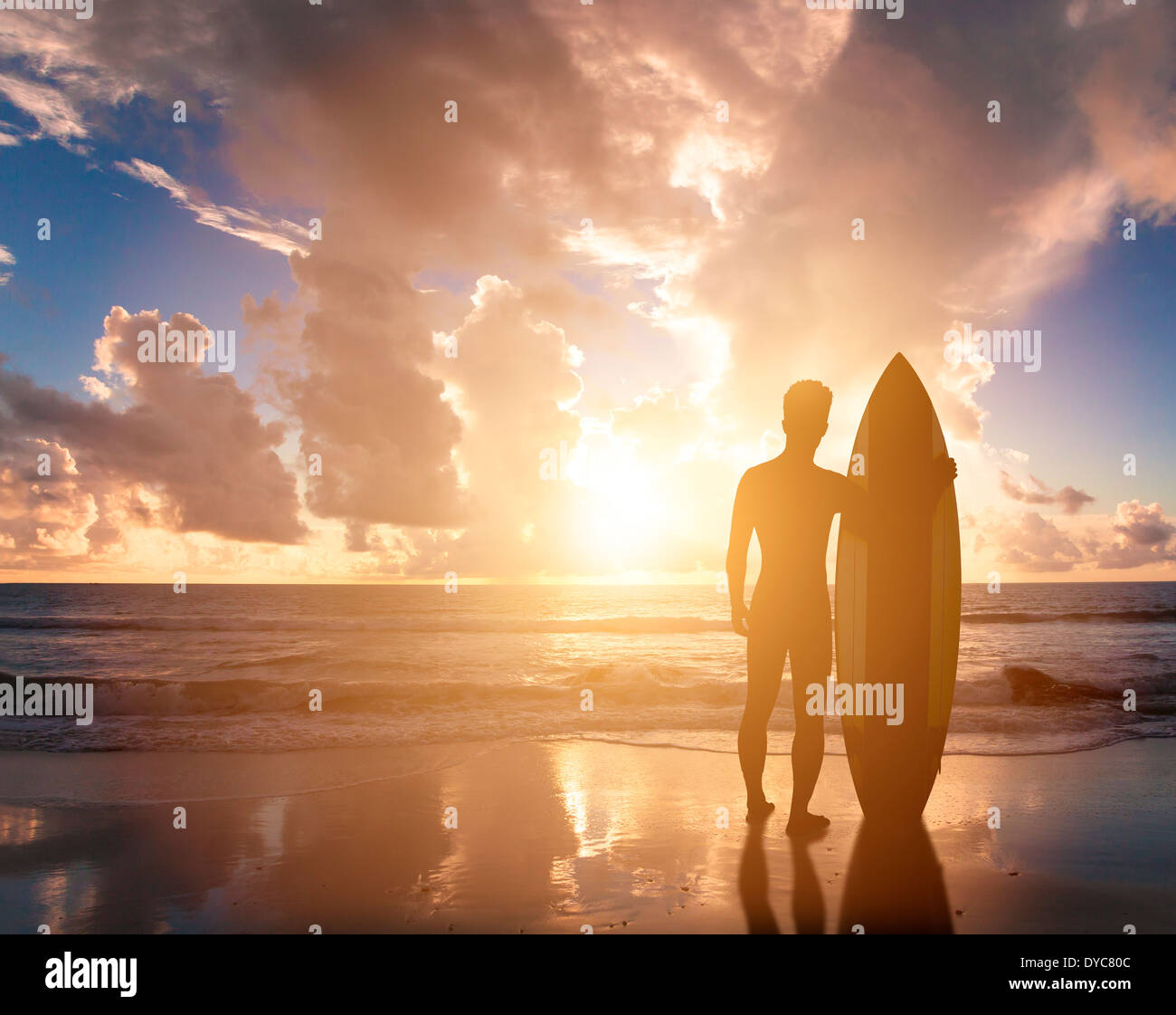 Surfer homme debout sur la plage en regardant le lever du soleil Banque D'Images