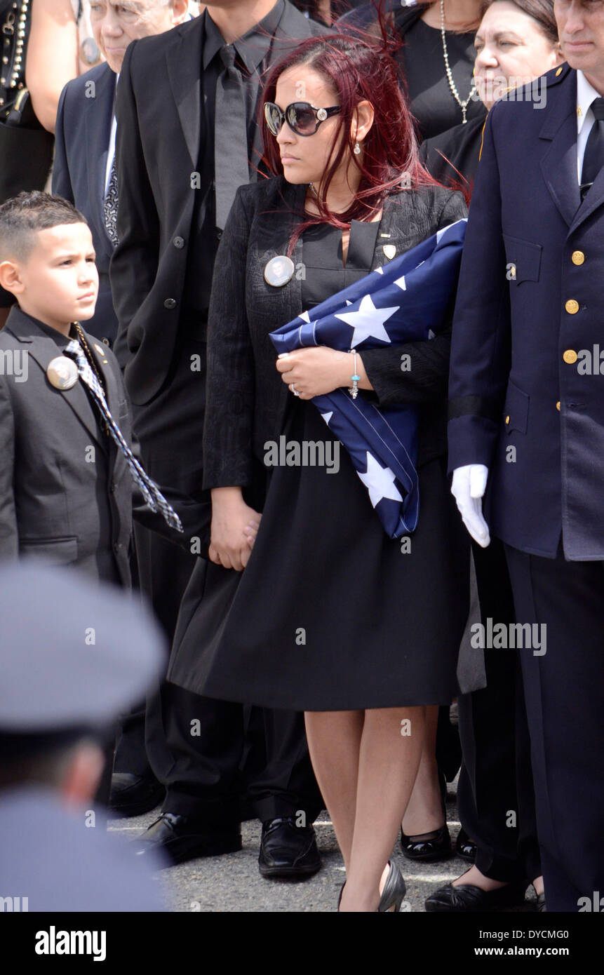 St Rose de Lima RC, NY, USA. 14 avril, 2014. Femme de PO Guerra, agent de police tués dans un incendie en Coney Island Projet de logement nous tient d'un drapeau comme elle se tient avec son fils en face de l'église. Crédit : Michael Glenn/Alamy Live News Banque D'Images