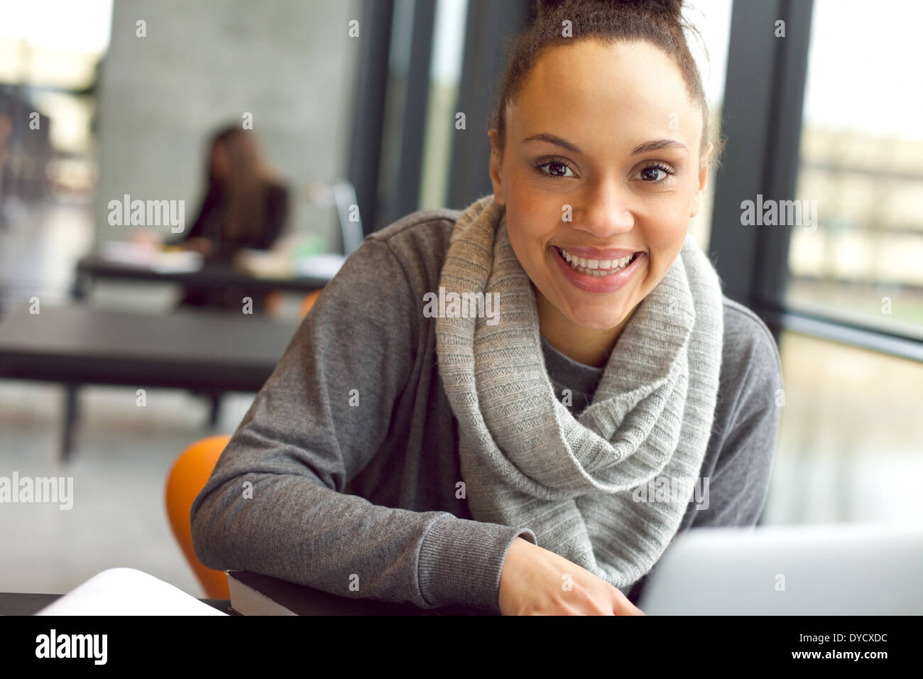 Close up portrait of young African woman sitting in library smiling at camera. Female student in university library. Banque D'Images