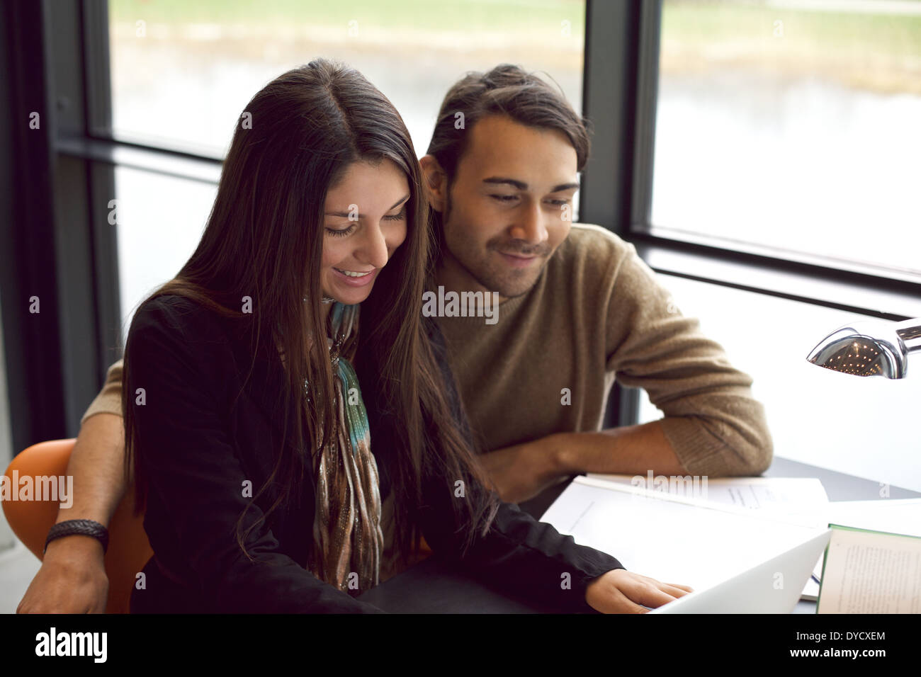 Deux jeunes étudiants assis ensemble à table à l'aide d'ordinateur portable. Camarades de classe avec des livres et l'ordinateur portable pour trouver de l'information. Banque D'Images
