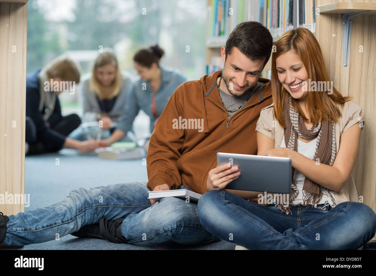 Smiling students using tablet avec vos amis en arrière-plan à bibliothèque Banque D'Images