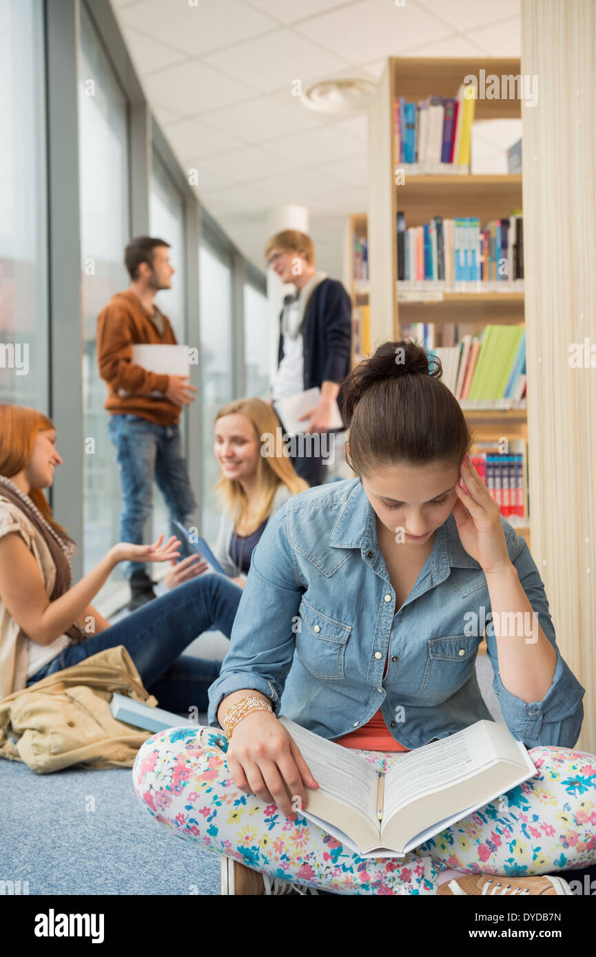 Girl reading book avec groupe d'étudiants discutant in library Banque D'Images