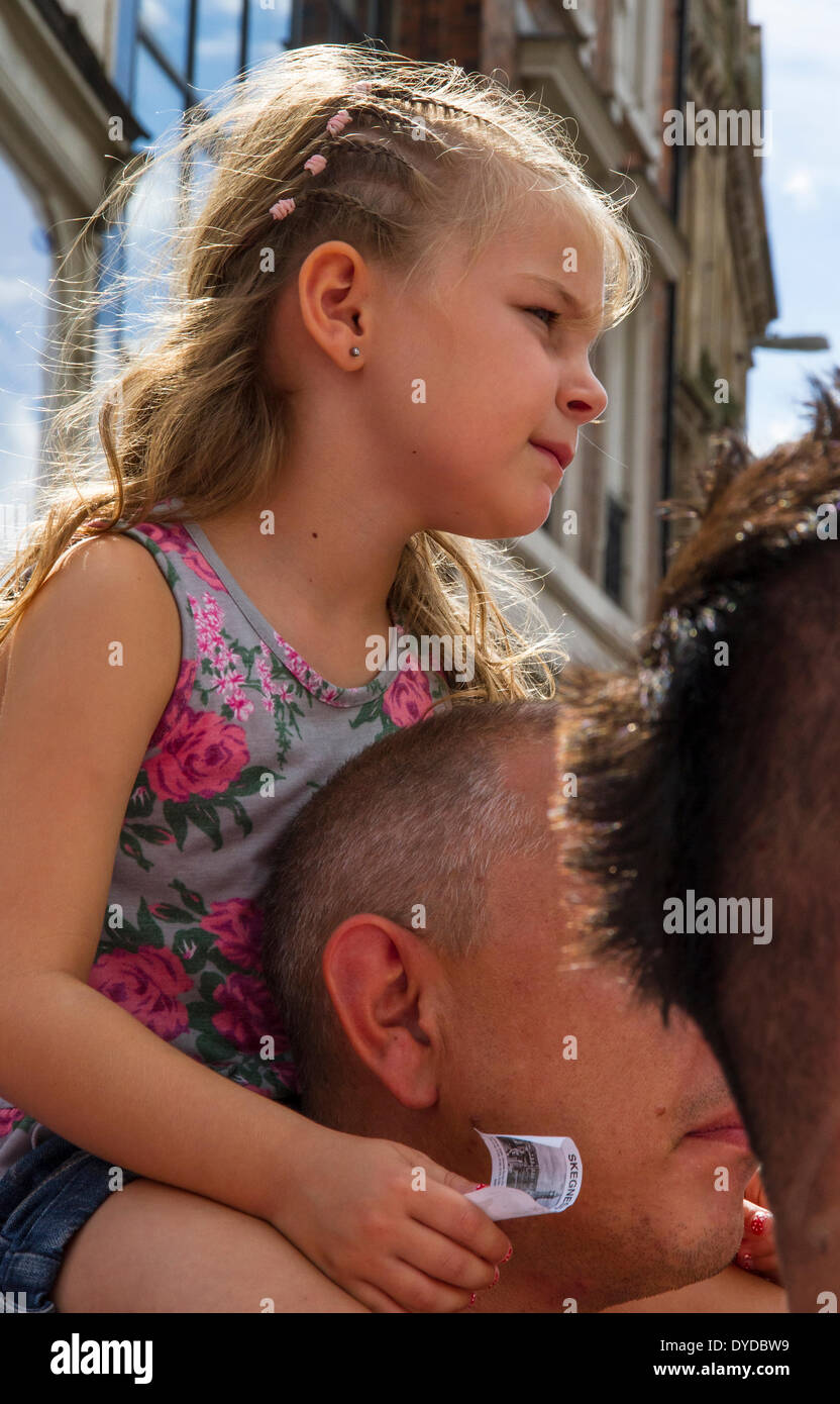 Jeune fille sur les épaules de son père pour qu'elle puisse voir l'événement. Banque D'Images