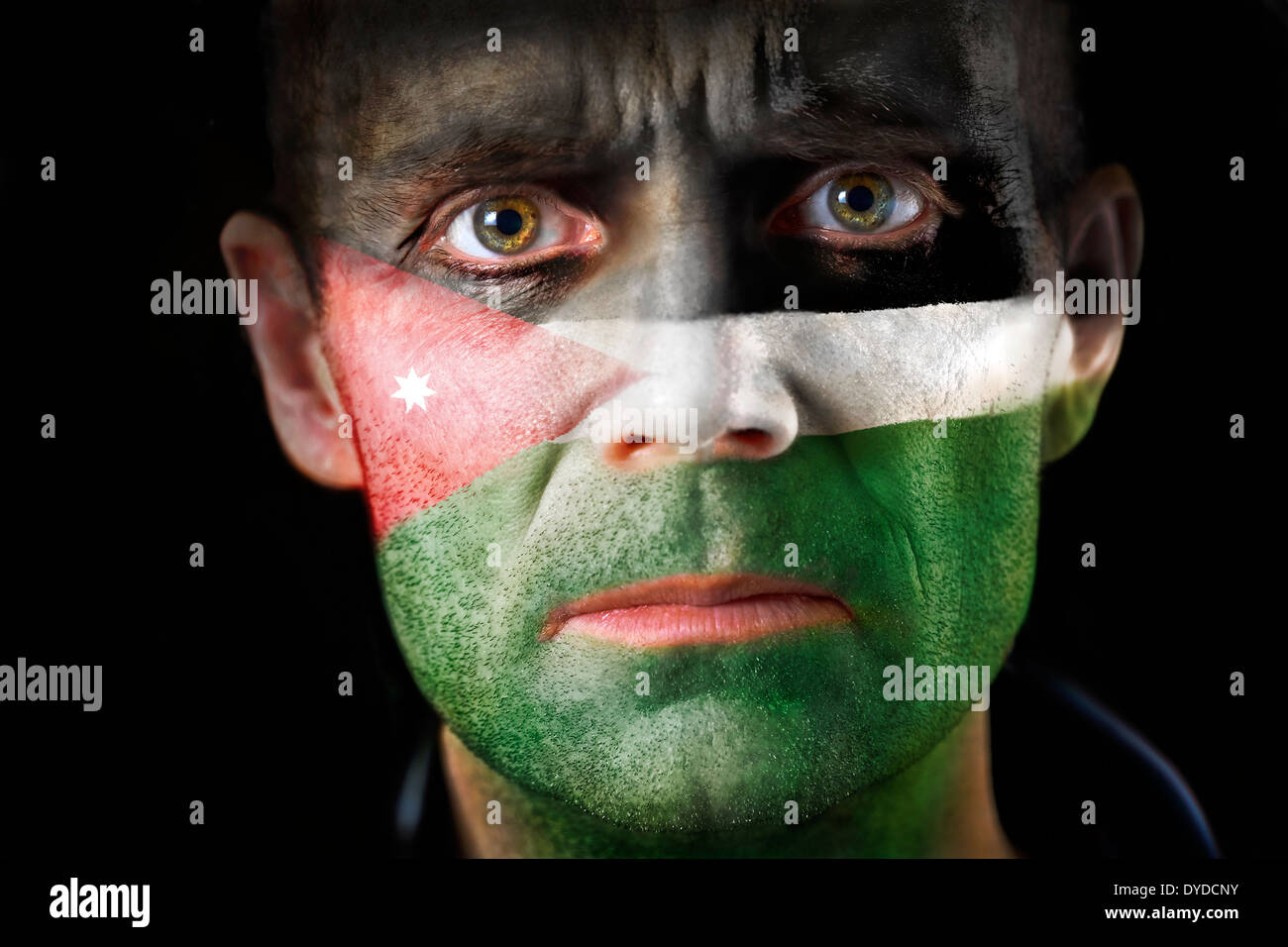 Un regard intense d'un homme avec le visage peint avec le drapeau jordanien. Banque D'Images