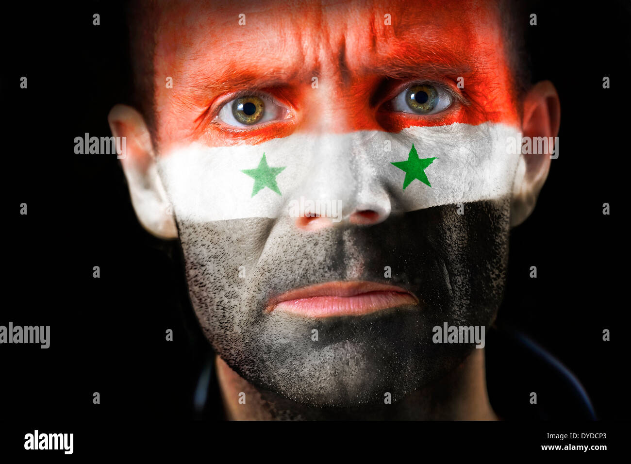 Un regard intense d'un homme avec le visage peint avec le drapeau syrien. Banque D'Images