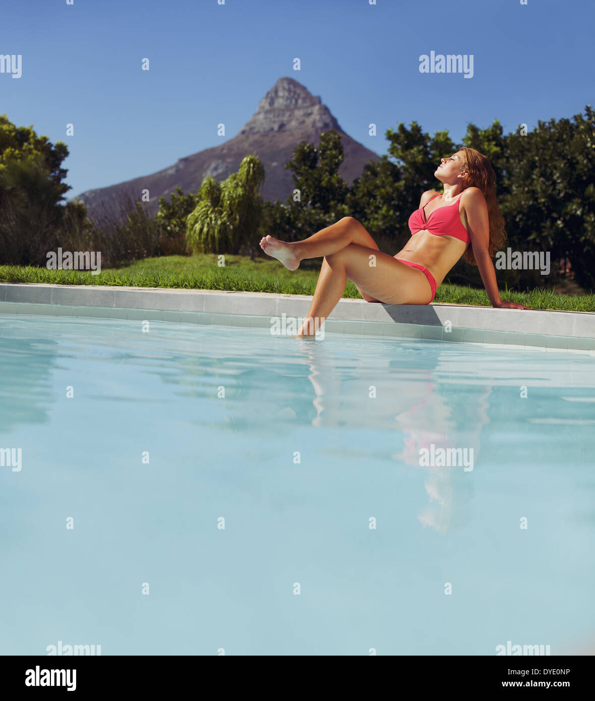 Belle jeune femme assise en piscine et profiter d'un bain de soleil. Portrait modèle féminin en bikini au soleil au bord de la piscine. Banque D'Images