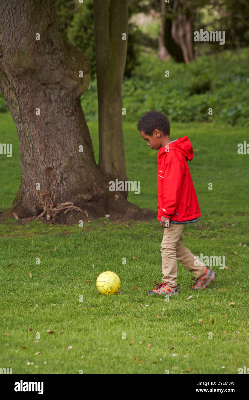 Jeune garçon en rouge haut botter un ballon Banque D'Images