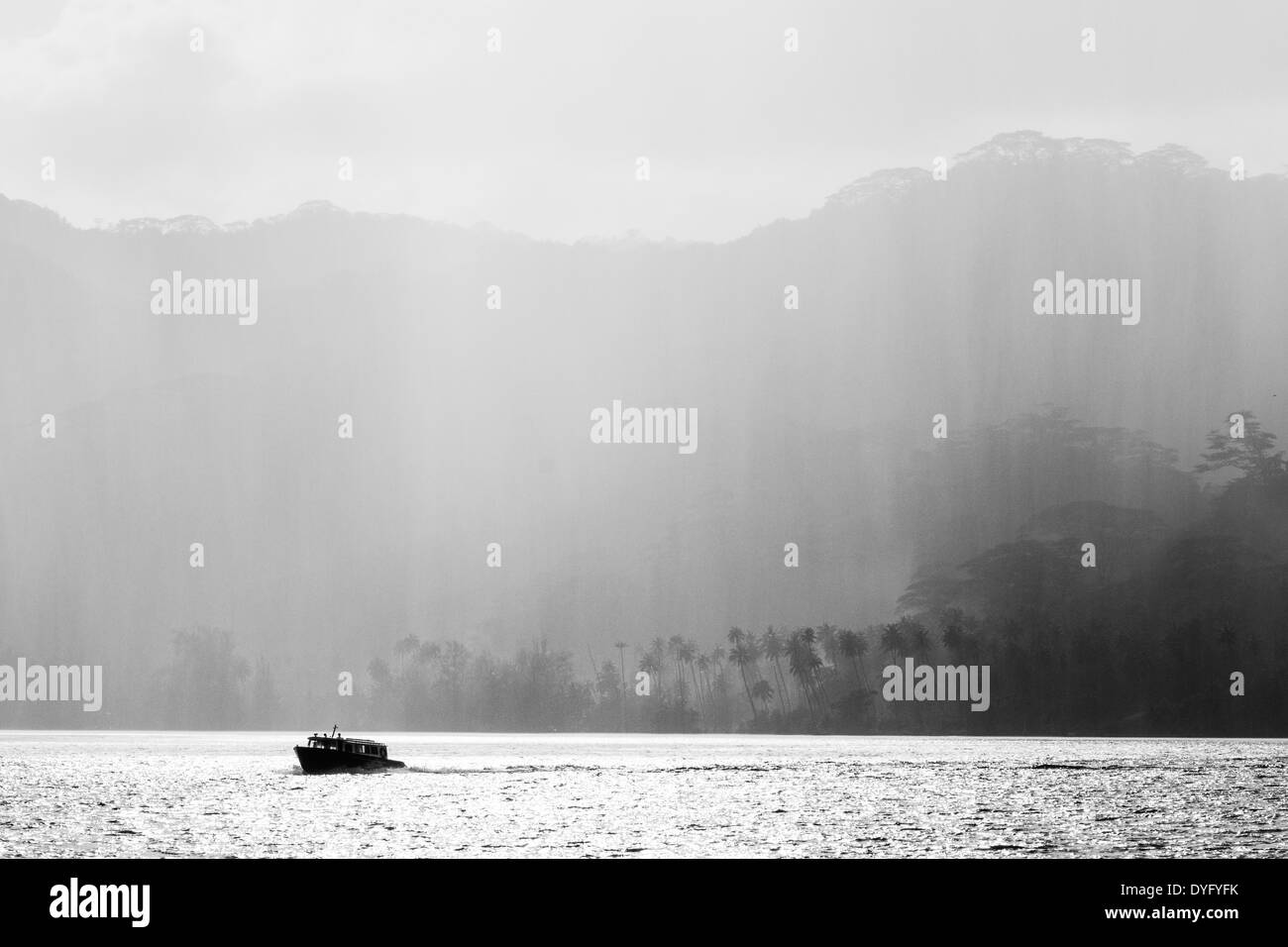 Silhouette de bateau contre douche pluie tomber sur les couches d'arbres tropicaux en polynésie francaise Banque D'Images