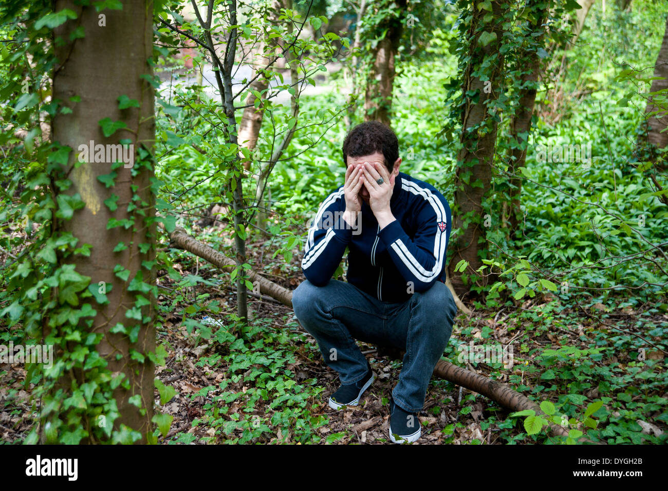 Un homme déprimé assis seul dans les bois avec la tête dans les mains Banque D'Images
