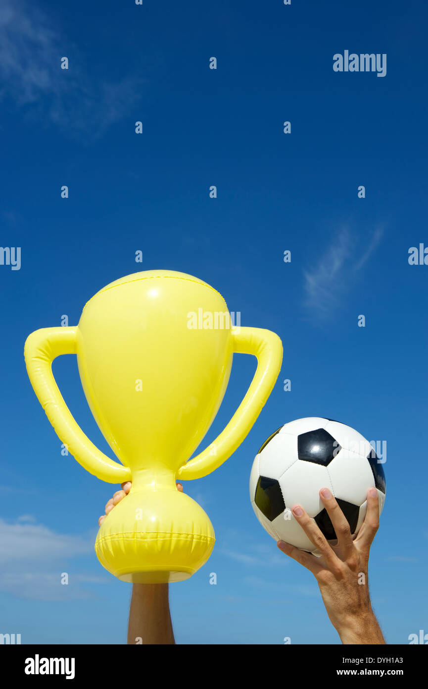 Mains de gagner champion football holding trophy jaune gonflable ballon de soccer et de ciel bleu Banque D'Images