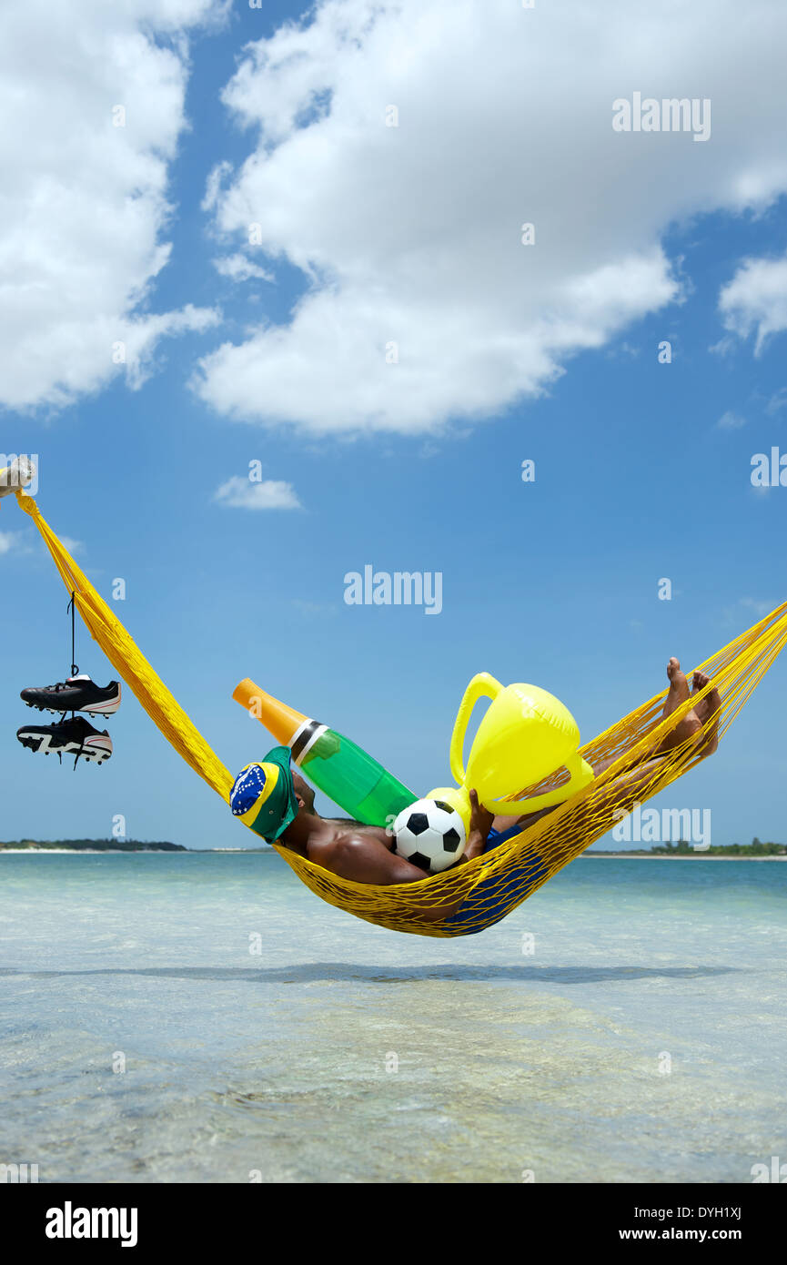 Le joueur de soccer brésilien Champion célébrer en vous relaxant dans son hamac avec football, bouteille de champagne, et le trophée Banque D'Images