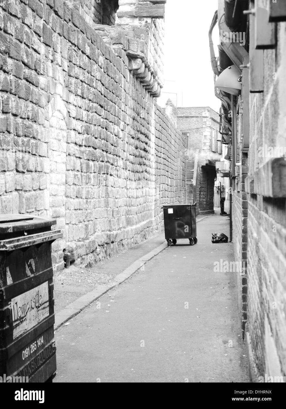 Image Monochrome - Urban street scène montrant wheelie les poubelles près de mur de la ville historique, Newcastle upon Tyne, England, UK Banque D'Images