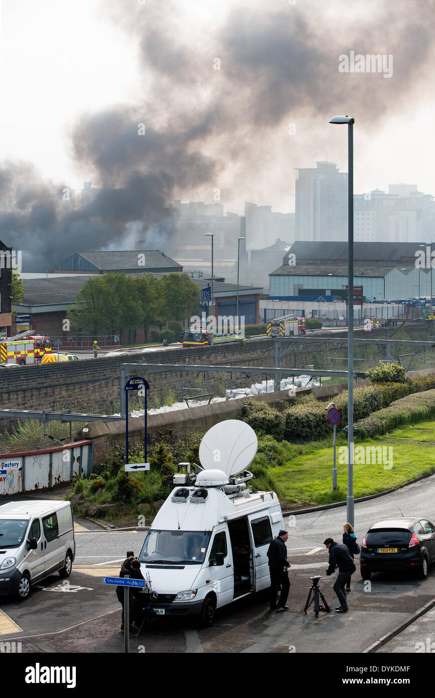Leeds, West Yorkshire, Royaume-Uni, 21 avril 2014. Armley Road. Une nappe de fumée flotte dans l'air que les pompiers s'attaquer à un grand feu dans une zone industrielle de Leeds. Derrière sont les développements résidentiels de grande hauteur dans et autour du centre-ville. L'incendie a éclaté à environ 1,50 heures dans les locaux d'Tradpak une usine de recyclage de l'emballage et de produits chimiques dans l'Armley de la ville. L'usine est à proximité du centre-ville et les résidants des environs ont été dit de garder leurs fenêtres et portes fermées à cause de produits chimiques potentiellement toxiques impliqués. Crédit : Ian Wray/Alamy Live News Banque D'Images