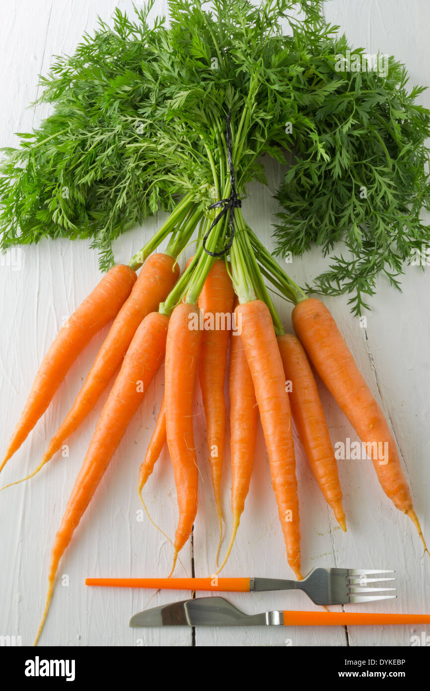 Un tas de carottes affiché sur un tableau blanc avec un couteau et fourchette. Un légume racine populaire plein de vitamine A. Banque D'Images