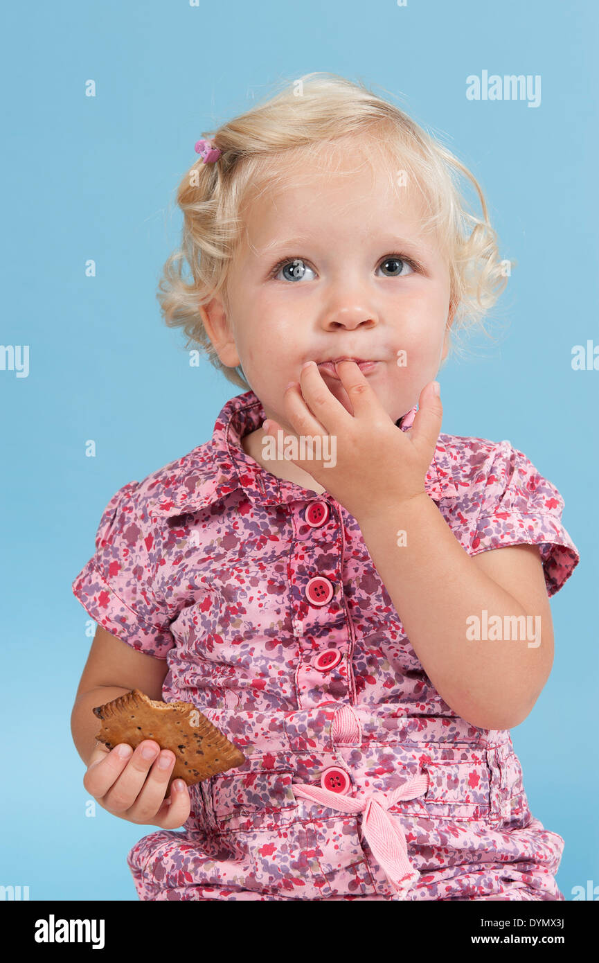 Petite fille de manger un biscuit. Isolé sur fond bleu Banque D'Images