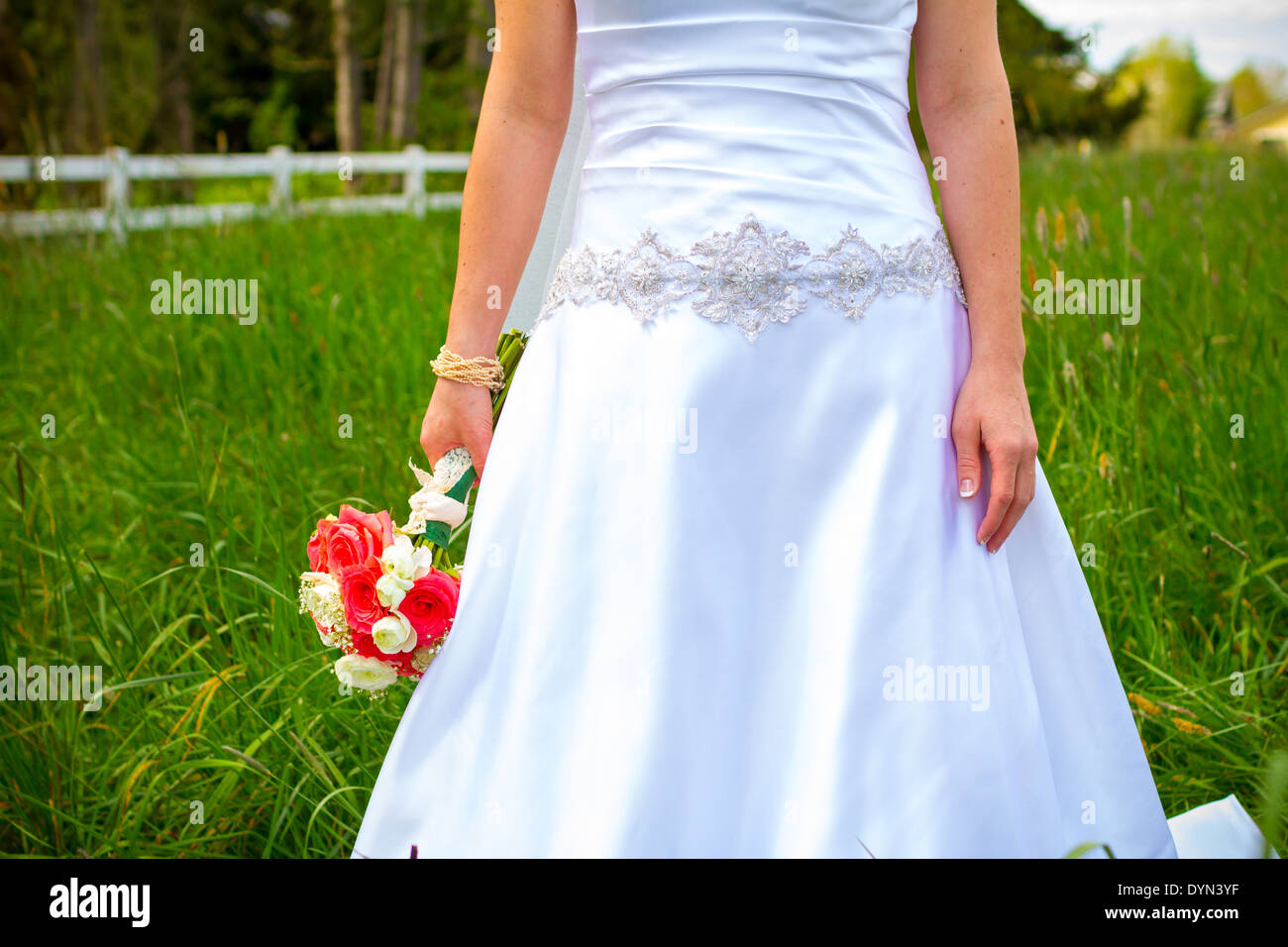 Promise dans son robe de mariée blanche tenant un beau bouquet de fleurs roses notamment. Banque D'Images