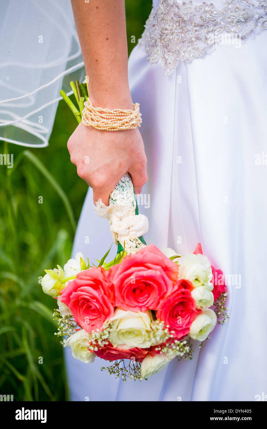 Promise dans son robe de mariée blanche tenant un beau bouquet de fleurs roses notamment. Banque D'Images