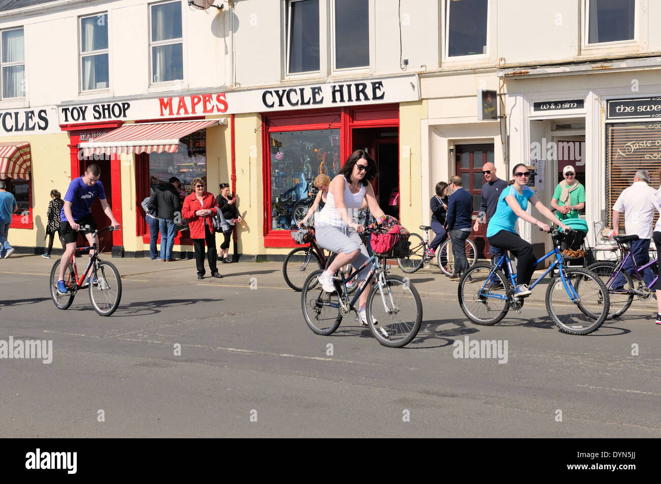Visiteurs à participer à la ronde du cycle traditionnel de l'île de (Cumbrae). Dans l'arrière-plan est un service de location de vélos et Mapes toy shop à Millport, Ecosse, Royaume-Uni Banque D'Images