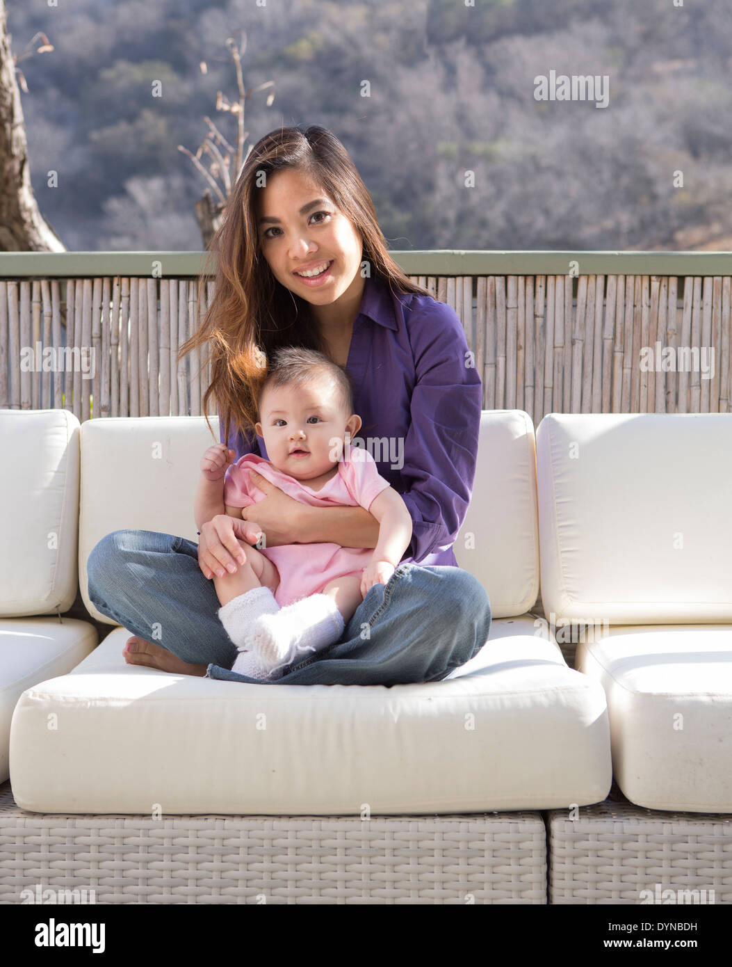 Mother holding baby girl on patio sofa Banque D'Images