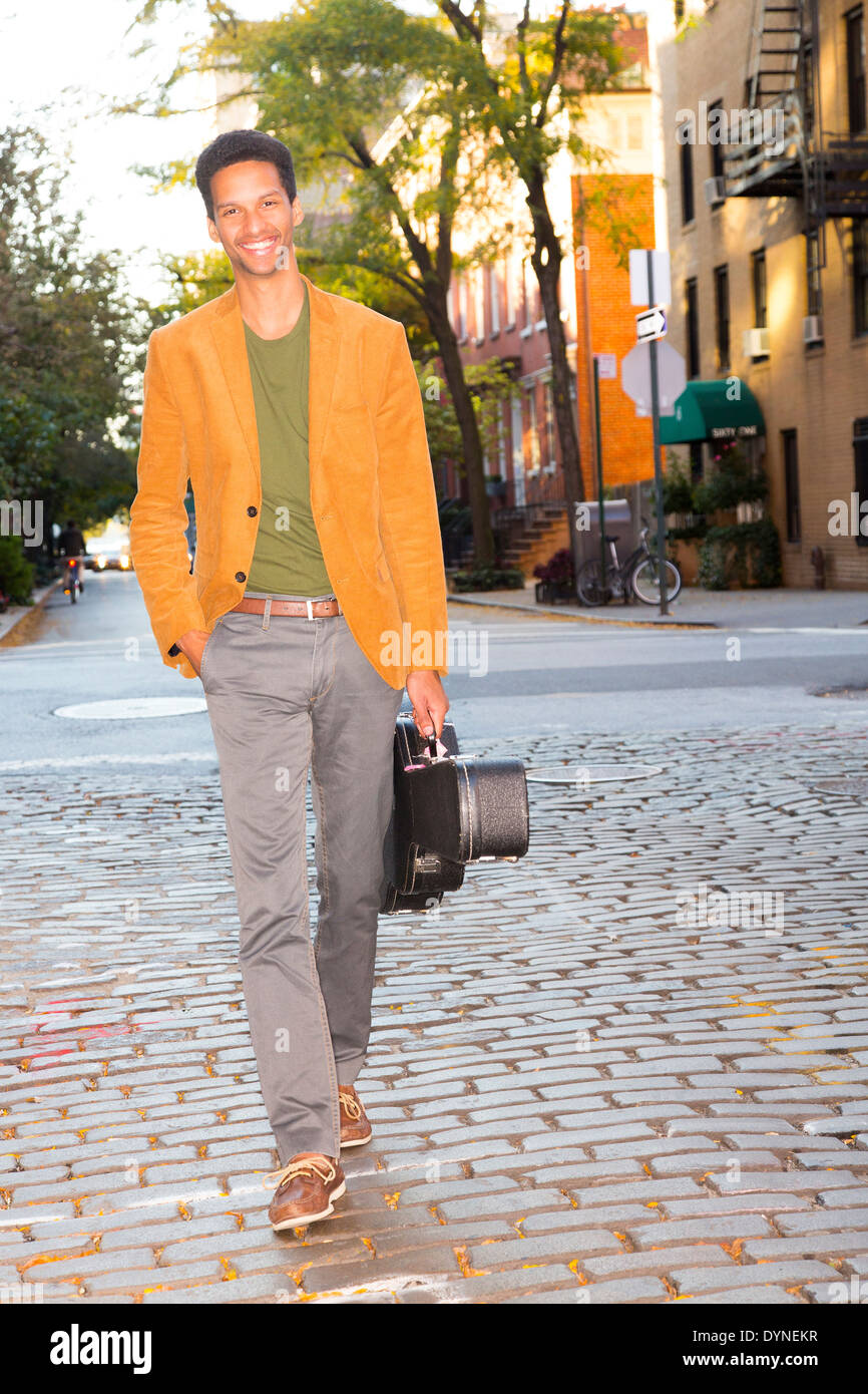 Mixed Race man carrying guitar on city street Banque D'Images