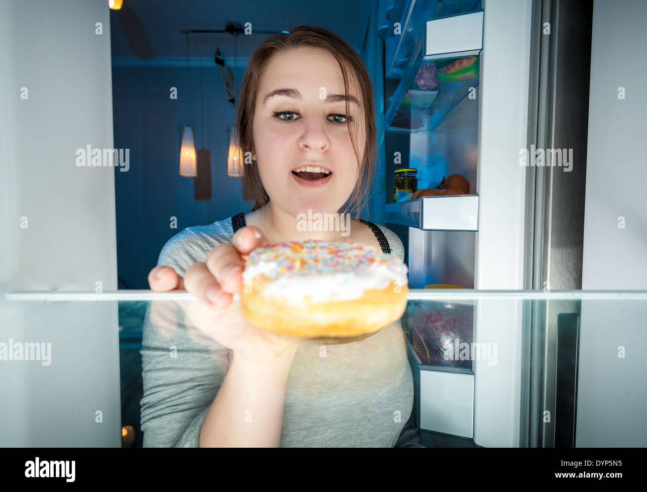 Closeup portrait of young woman taking donut hors du réfrigérateur pendant la nuit Banque D'Images