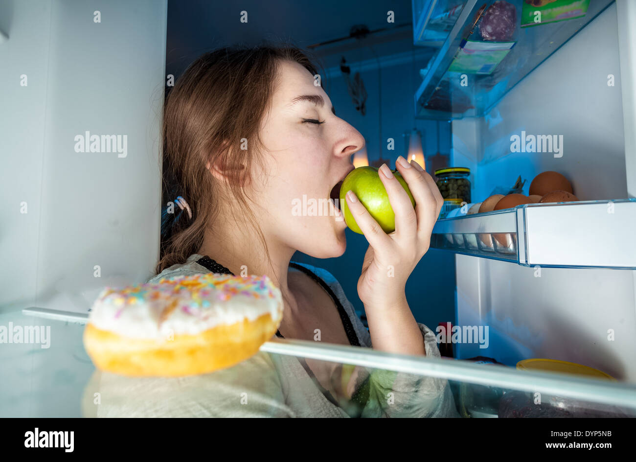 Closeup portrait de l'intérieur du réfrigérateur de young woman eating apple Banque D'Images