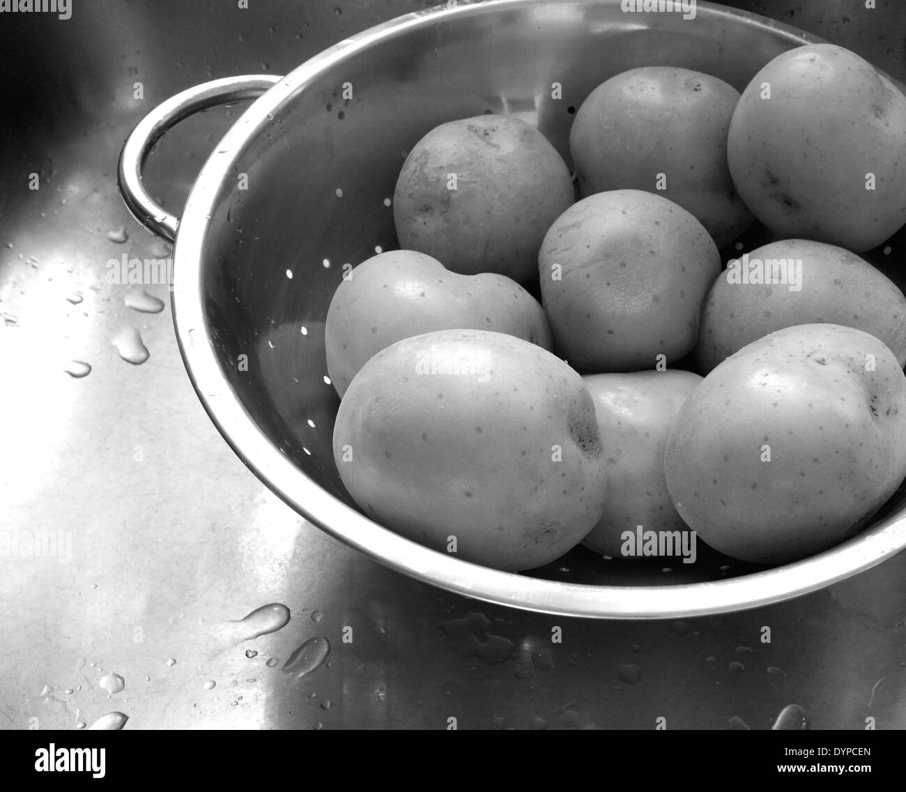 Photographie en noir et blanc d'éplucher des pommes de terre à l'eau de refroidissement dans une passoire. Banque D'Images