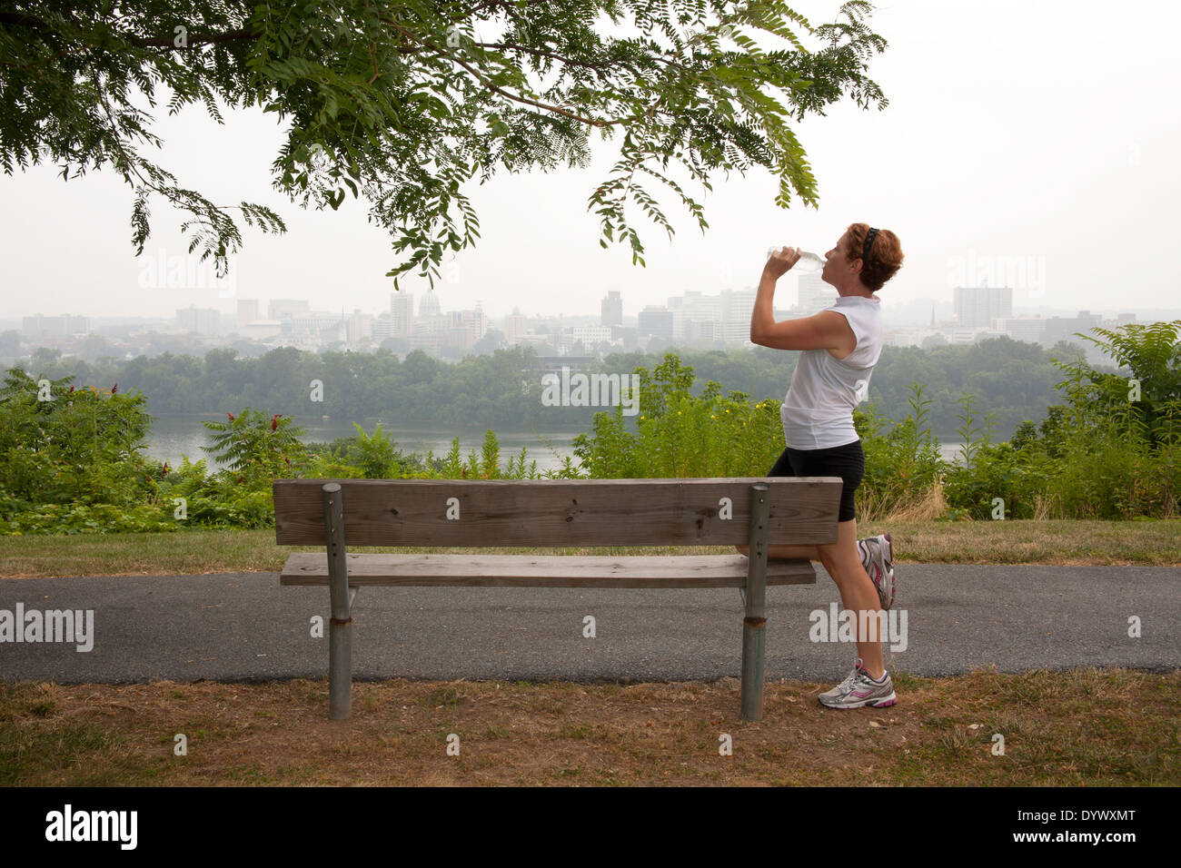 Femme mature de prendre une pause et de l'eau potable par le jogging sur un banc de parc avec vue sur la ville Banque D'Images
