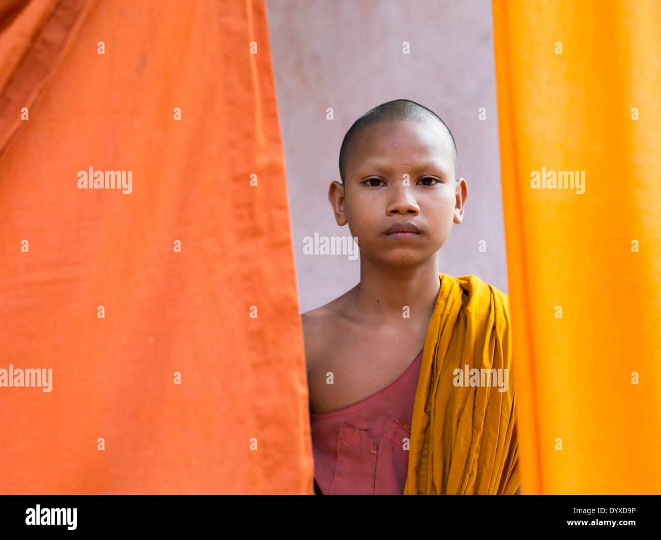 Jeune moine debout parmi les robes orange qui sont en train de sécher dehors. Angkor Wat, Siem Reap, Cambodge Banque D'Images