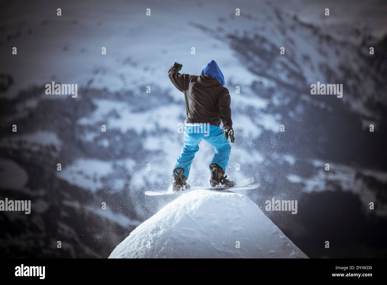 Snowboarder vêtu d'un sweat, tourne sur un dôme de neige avec des montagnes en arrière-plan. Banque D'Images