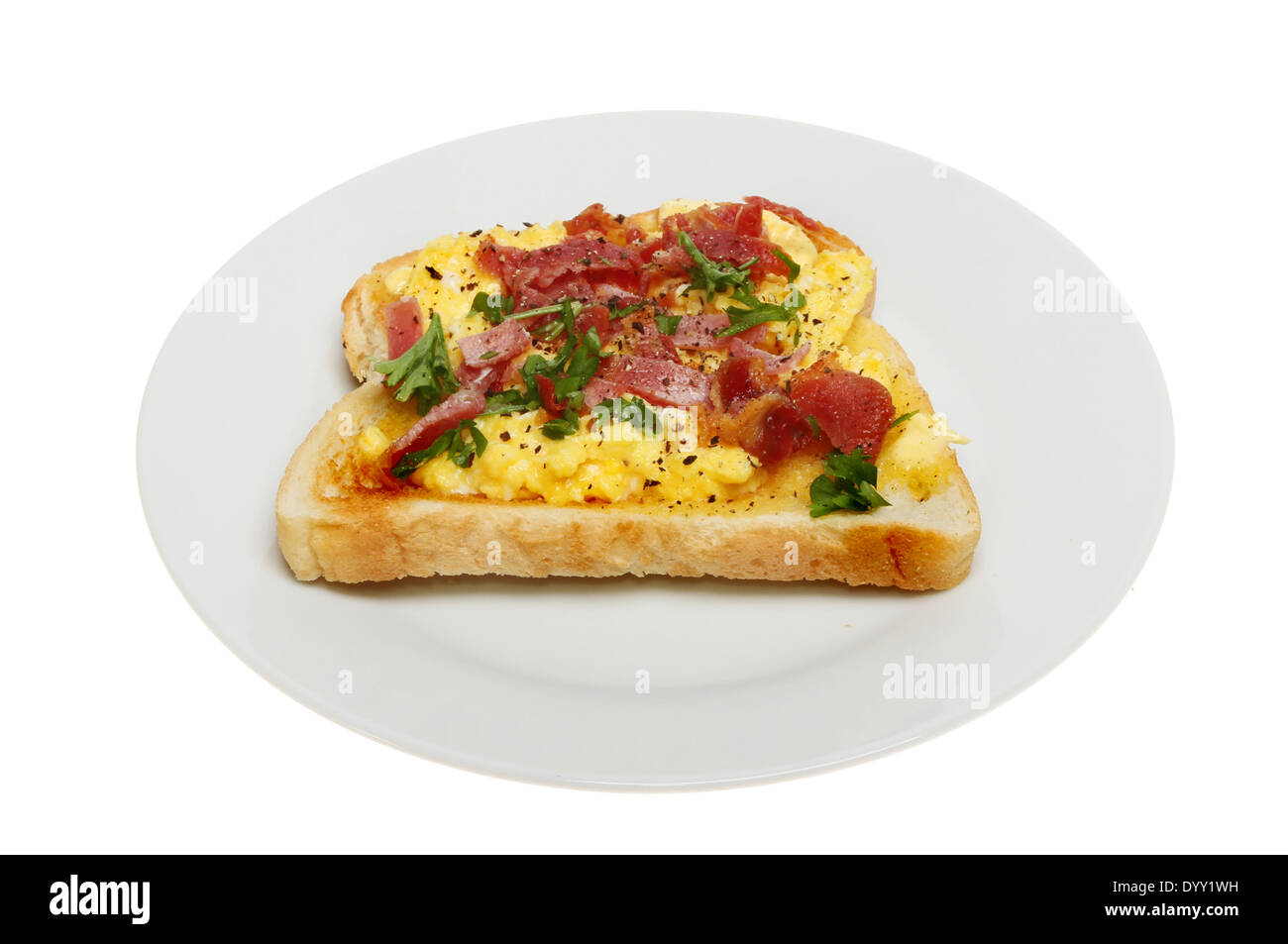 Oeufs brouillés avec bacon croustillant et le persil sur toast sur une assiette blanche contre isolés Banque D'Images