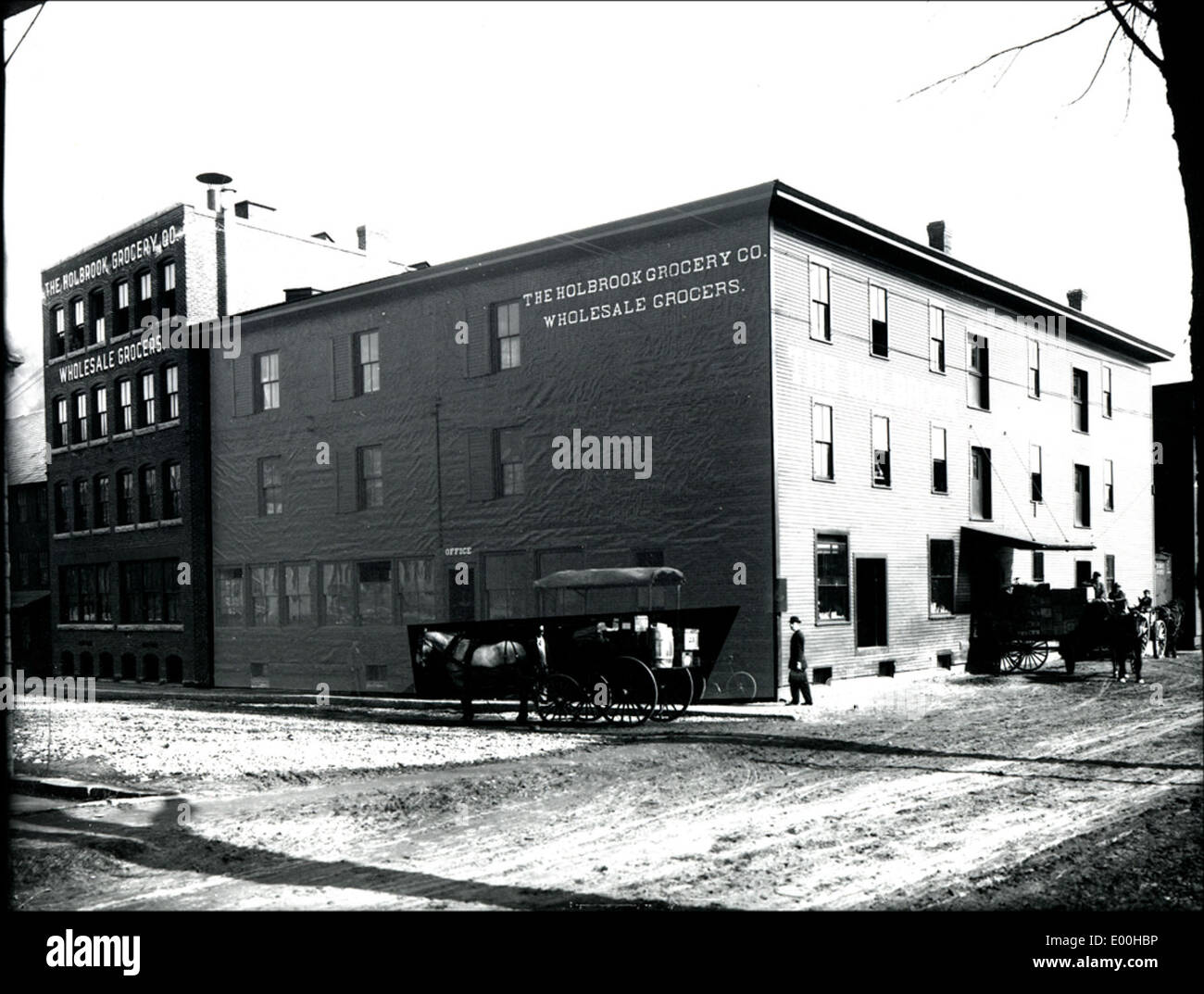La Holbrook Grocery Company, située sur Gilbo Avenue à Keene, New Hampshire, est représentée sur cette image historique. La photographie capture l'épicerie et un cheval et une poussette, reflétant les pratiques de transport et d'affaires de l'époque au début du XXe siècle. Banque D'Images