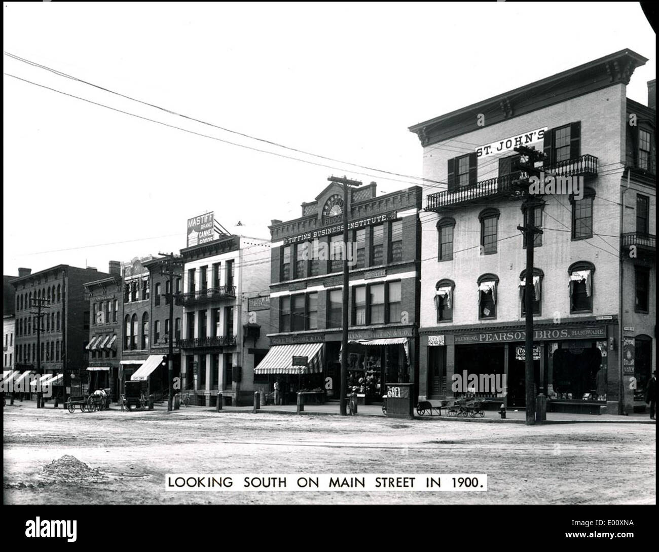 Cette photographie historique de main Street à Keene, New Hampshire, prise au début des années 1900, montre le centre-ville animé avec des calèches, des boutiques et le Tiffin's Business Institute. L'image capture le quartier animé des affaires et le charme de l'époque avec son architecture vintage et son activité piétonne. Banque D'Images