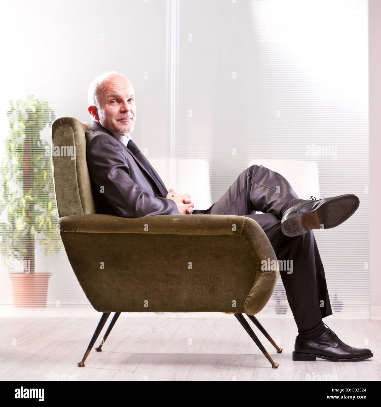 Mature businessman assis sur un fauteuil très confortable et relaxant vous sourit ! Banque D'Images