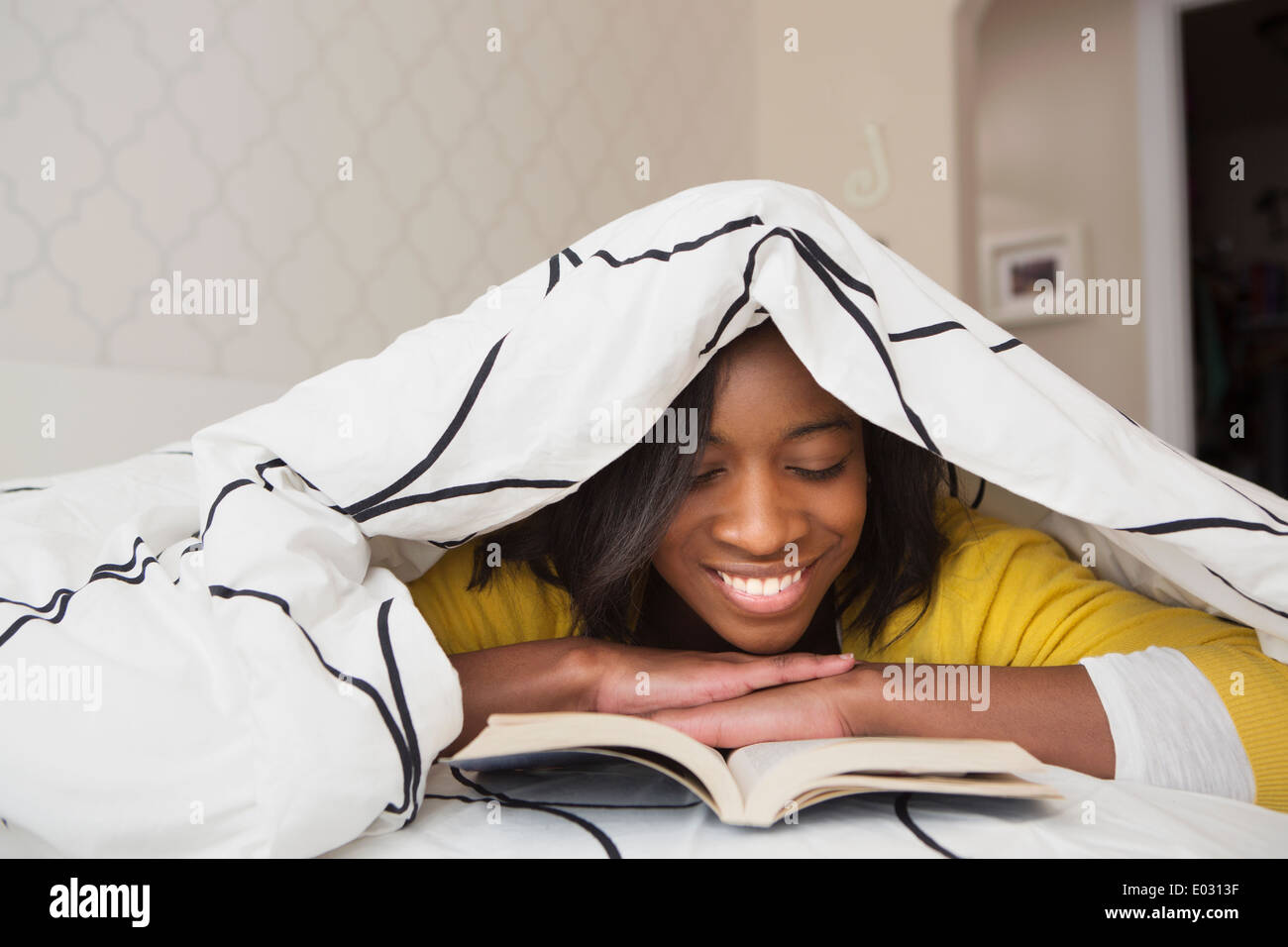 Une jeune fille dans son lit sous une couette en lisant un livre Photo  Stock - Alamy