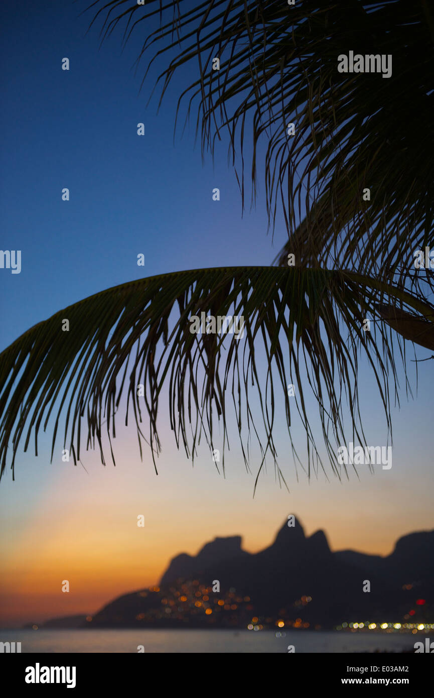 Rio de Janeiro Ipanema Beach Brésil coucher du soleil avec le scintillement des lumières de favela Vidigal et deux frères montagne sous palm tree Banque D'Images