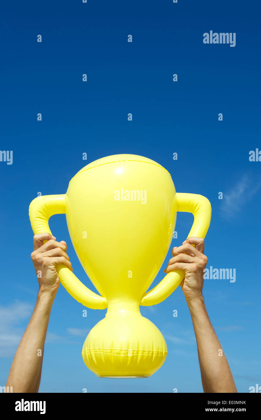 Mains de champion gagnant holding trophy jaune gonflable dans ciel bleu Banque D'Images