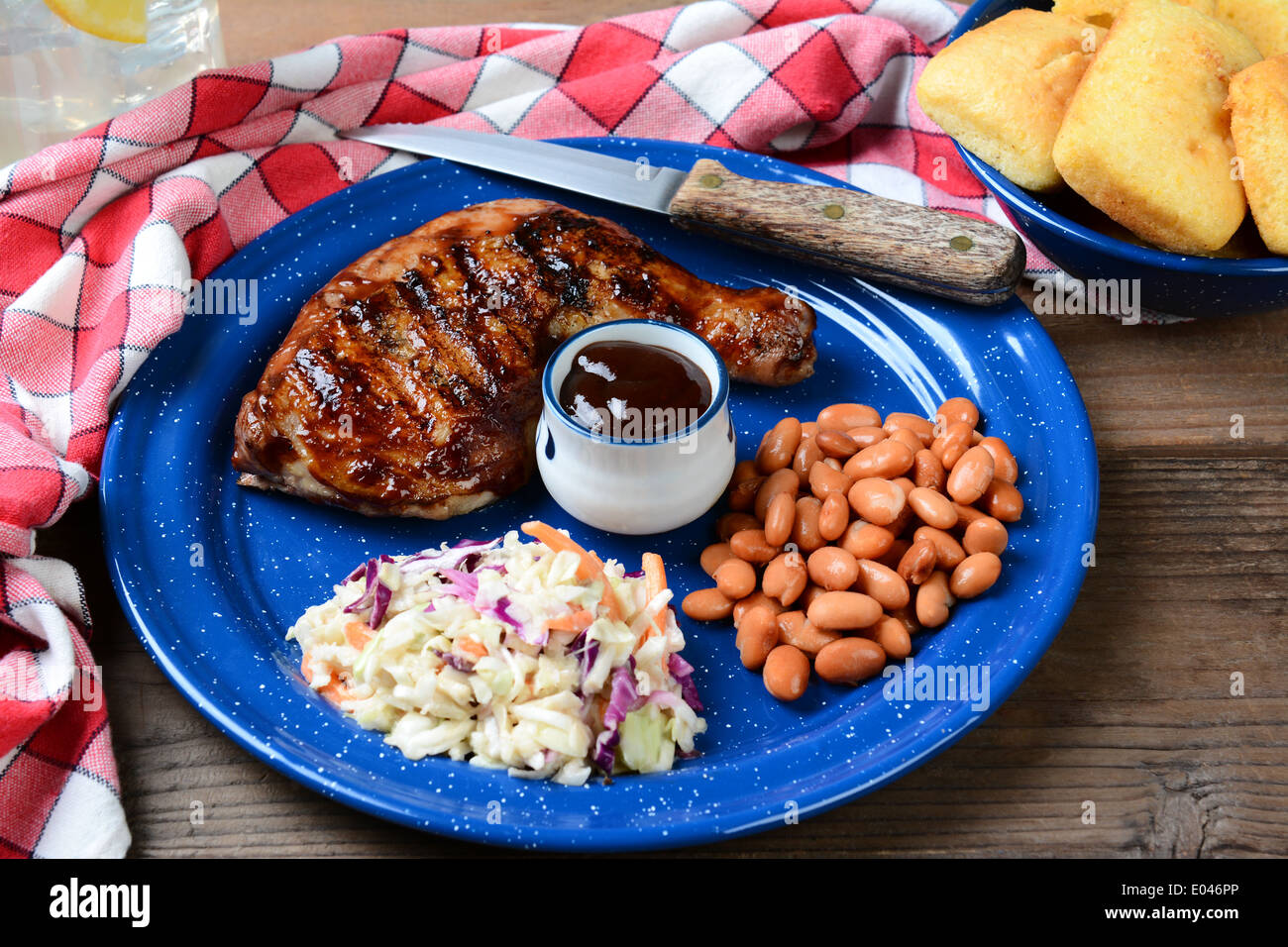 Un gros plan de la plaque du poulet barbecue avec cole slaw, les haricots pinto et le pain de maïs. Le repas est sur une table de restaurant rustique en bois Banque D'Images